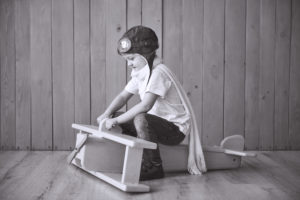 Happy kid in pilot hat playing with wooden airplane against. Childhood. Fantasy, imagination. Holiday.